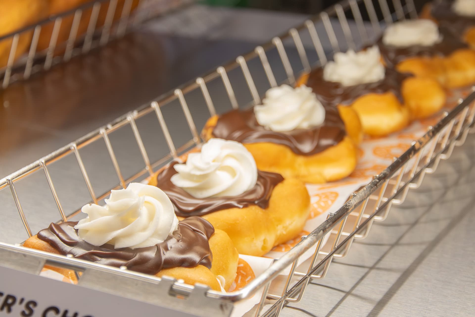 Golden donuts with chocolate and white cream toppings arranged in a wire basket on white paper.
